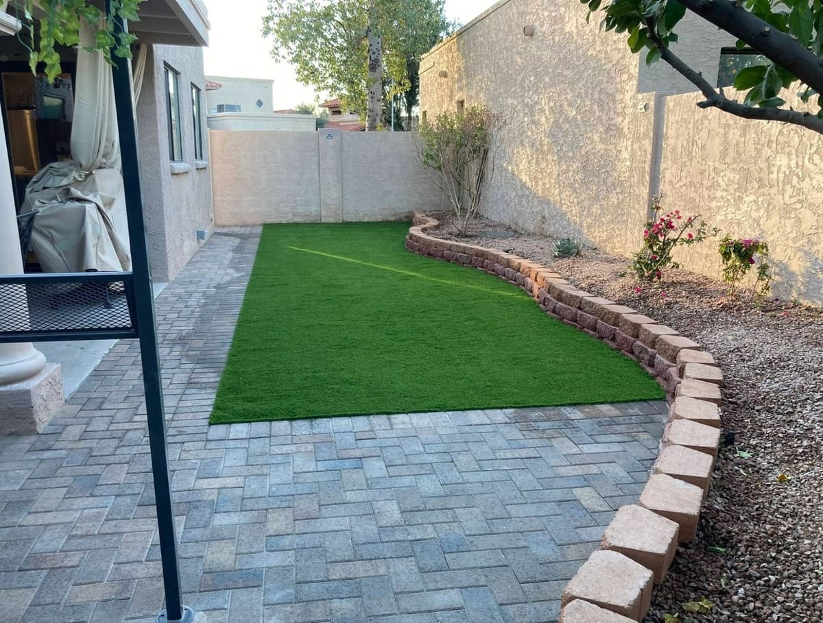 After: artificial turf installed and the patio finished in pavers along a curved block border