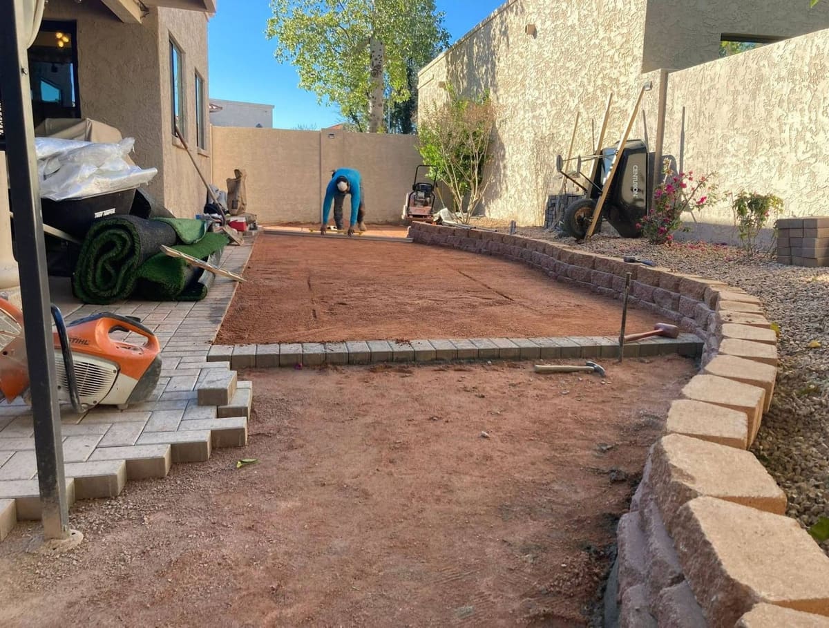 Before: bare compacted base inside a new paver border, with turf rolls and tools on site