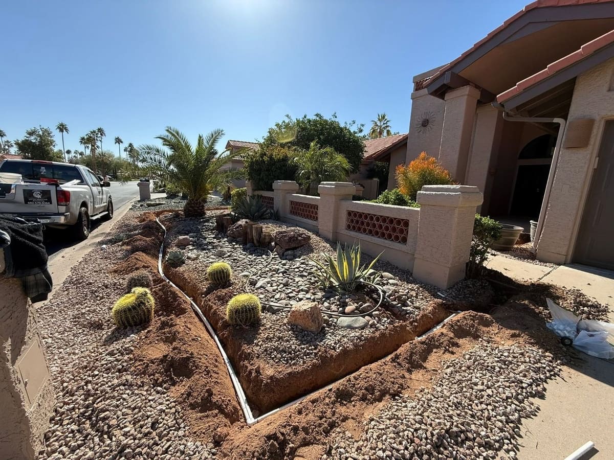 Front-yard desert landscape with barrel cactus, agave and river rock, with new irrigation trenches