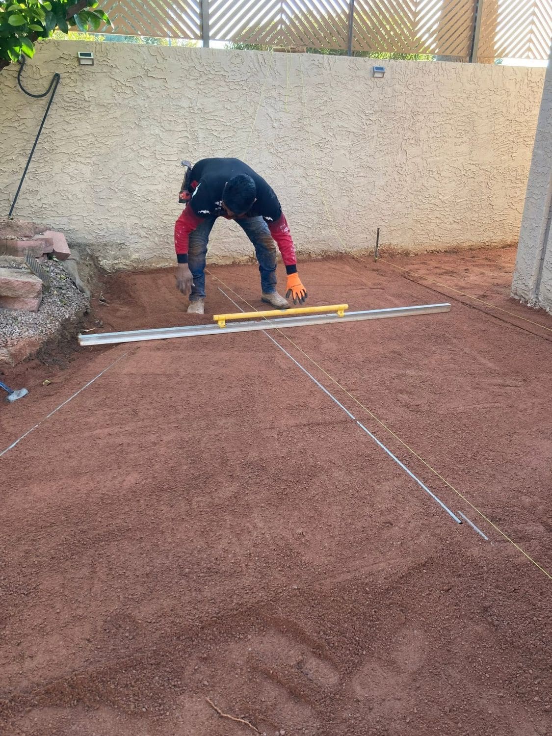 Crew member screeding a sand base flat with a long aluminum rail and string lines