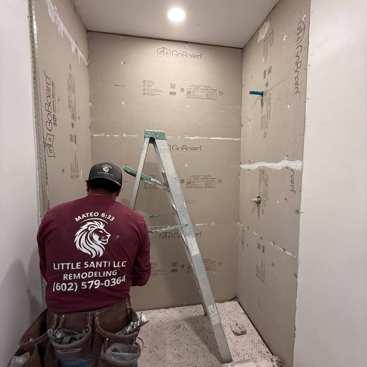 Crew member in a Little Santi shirt inside a shower boarded with waterproof wall panels