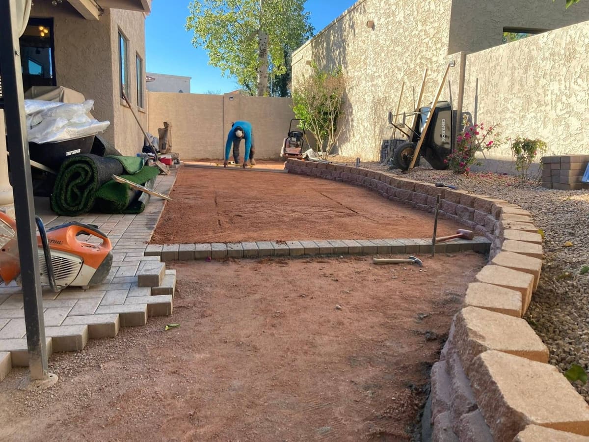 Backyard with a leveled base ready for turf, rolls of artificial turf staged beside the patio