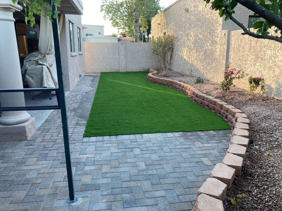 Finished backyard: green artificial turf framed by gray-blend pavers and a curved block border